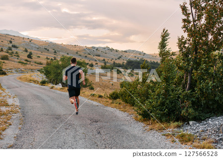 Determined Athlete Running Through Rugged Mountain Terrain at Sunrise. 127566528