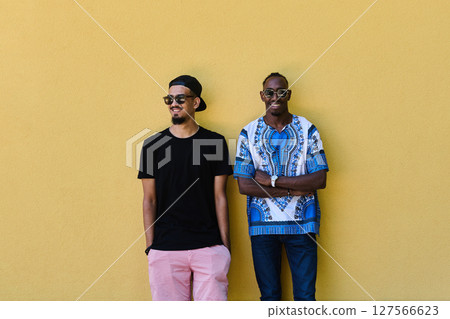 Two Male Friends: African American Teenager in Sudanese Traditional Attire Leaning Against Yellow Wall 127566623
