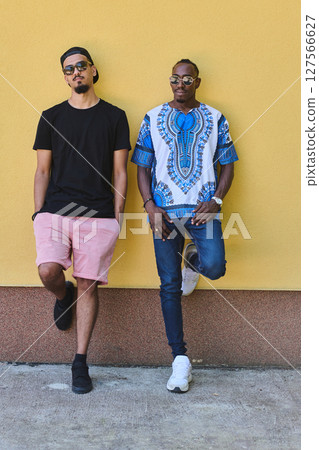 Two Male Friends: African American Teenager in Sudanese Traditional Attire Leaning Against Yellow Wall Two Male Friends: African American Teenager in Sudanese Traditional Attire Leaning Against Yellow Wall 127566627