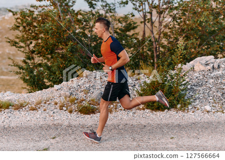 Determined Athlete Running Through Rugged Mountain Terrain at Sunrise. Determined Athlete Running Through Rugged Mountain Terrain at Sunrise. 127566664