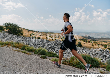 Determined Athlete Running Through Rugged Mountain Terrain at Sunrise. 127566665