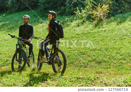 A blissful couple, adorned in professional cycling gear, enjoys a romantic bicycle ride through a park, surrounded by modern natural attractions, radiating love and happiness 127566719