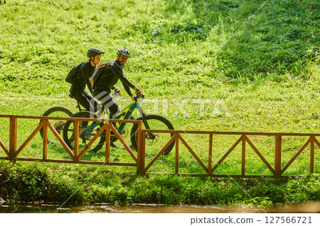 A blissful couple, adorned in professional cycling gear, enjoys a romantic bicycle ride through a park, surrounded by modern natural attractions, radiating love and happiness A blissful couple, adorned in professional cycling gear, enjoys a romantic bicycle ride through a park, surrounded by modern natural attractions, radiating love and happiness 127566721