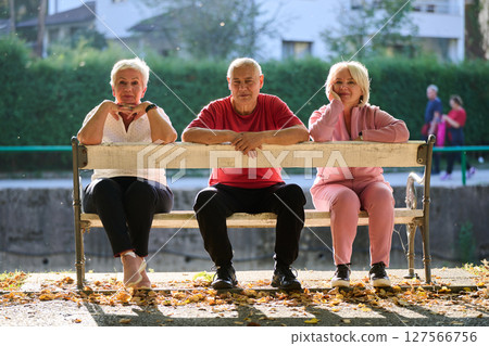 A group of elderly individuals, including a senior man and two older women, sits in a park on a sunny autumn day, embodying the concept of healthy aging through companionship, relaxation, and outdoor 127566756