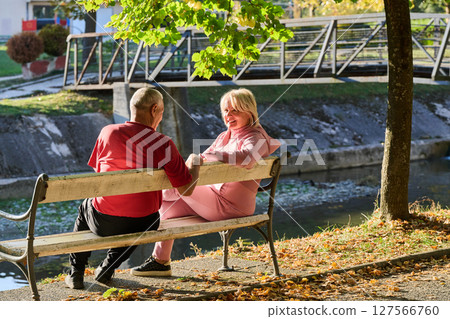 Elderly couple finding solace and joy as they rest on a park bench, engaged in heartfelt conversation, following a rejuvenating strol a testament to the enduring companionship and serene connection 127566760