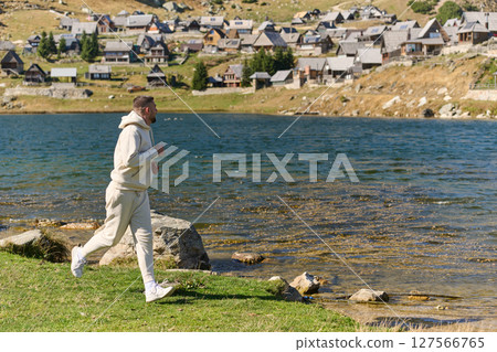 Athletic man maintains his healthy lifestyle by running through the scenic mountain and lakeside environment, showcasing a commitment to fitness and well-being 127566765