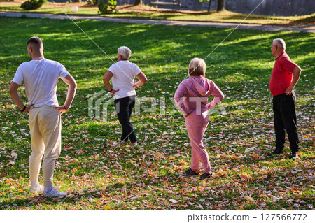 A group of seniors follows a trainer, engaging in outdoor exercises in the park, as they collectively strive to maintain vitality and well-being, embracing an active and health-conscious lifestyle in 127566772