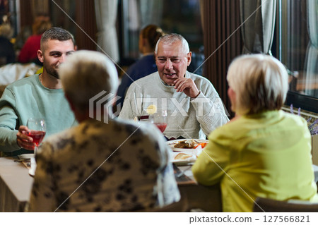 A group of family friends, comprising a young grandson and older individuals, share a delightful dinner in a modern restaurant, exemplifying the concept of healthy aging through intergenerational 127566821