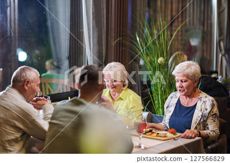 A group of family friends, comprising a young grandson and older individuals, share a delightful dinner in a modern restaurant, exemplifying the concept of healthy aging through intergenerational 127566829