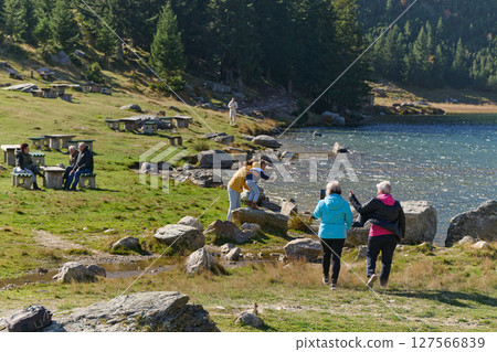 A family shares delightful moments with their friends amid the stunning landscapes of mountains, lakes, and winding paths, promoting a healthy lifestyle and the joy of familial bonds in the embrace of 127566839