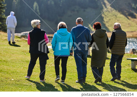 A family shares delightful moments with their friends amid the stunning landscapes of mountains, lakes, and winding paths, promoting a healthy lifestyle and the joy of familial bonds in the embrace of 127566854