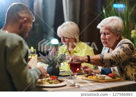 A group of family friends, comprising a young grandson and older individuals, share a delightful dinner in a modern restaurant, exemplifying the concept of healthy aging through intergenerational 127566863