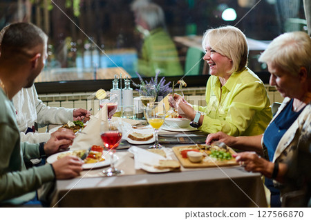 A group of family friends, comprising a young grandson and older individuals, share a delightful dinner in a modern restaurant, exemplifying the concept of healthy aging through intergenerational 127566870