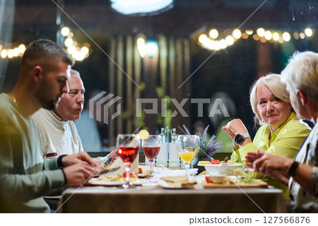 A group of family friends, comprising a young grandson and older individuals, share a delightful dinner in a modern restaurant, exemplifying the concept of healthy aging through intergenerational 127566876
