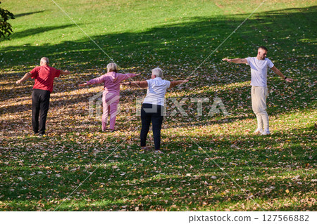 A group of seniors follows a trainer, engaging in outdoor exercises in the park, as they collectively strive to maintain vitality and well-being, embracing an active and health-conscious lifestyle in 127566882