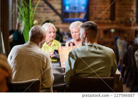 A group of family friends, comprising a young grandson and older individuals, share a delightful dinner in a modern restaurant, exemplifying the concept of healthy aging through intergenerational 127566887