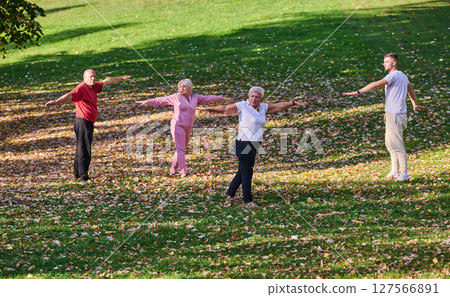 A group of seniors follows a trainer, engaging in outdoor exercises in the park, as they collectively strive to maintain vitality and well-being, embracing an active and health-conscious lifestyle in A group of seniors follows a trainer, engaging in outdoor exercises in the park, as they collectively strive to maintain vitality and well-being, embracing an active and health-conscious lifestyle in 127566891