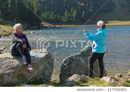 An elderly pair of women captures a timeless moment on their smartphones, blending technology with the serene beauty that surrounds them An elderly pair of women captures a timeless moment on their smartphones, blending technology with the serene beauty that surrounds them 127566902