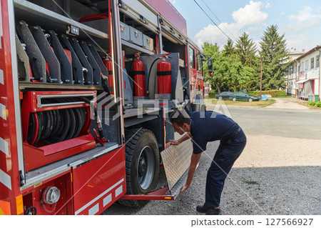A dedicated firefighter preparing a modern firetruck for deployment to hazardous fire-stricken areas, demonstrating readiness and commitment to emergency response 127566927