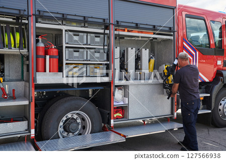 A dedicated firefighter preparing a modern firetruck for deployment to hazardous fire-stricken areas, demonstrating readiness and commitment to emergency response A dedicated firefighter preparing a modern firetruck for deployment to hazardous fire-stricken areas, demonstrating readiness and commitment to emergency response 127566938