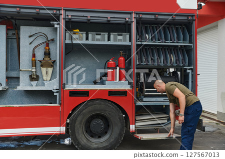A dedicated firefighter preparing a modern firetruck for deployment to hazardous fire-stricken areas, demonstrating readiness and commitment to emergency response 127567013