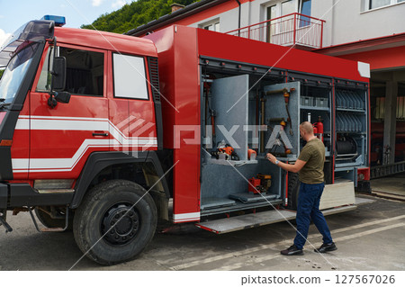 A dedicated firefighter preparing a modern firetruck for deployment to hazardous fire-stricken areas, demonstrating readiness and commitment to emergency response 127567026