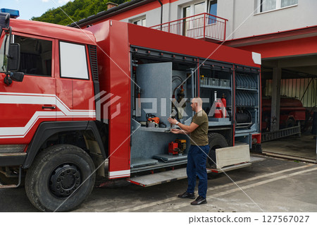 A dedicated firefighter preparing a modern firetruck for deployment to hazardous fire-stricken areas, demonstrating readiness and commitment to emergency response A dedicated firefighter preparing a modern firetruck for deployment to hazardous fire-stricken areas, demonstrating readiness and commitment to emergency response 127567027