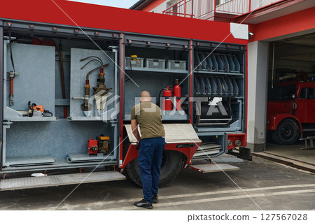 A dedicated firefighter preparing a modern firetruck for deployment to hazardous fire-stricken areas, demonstrating readiness and commitment to emergency response 127567028