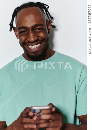 African American teenager engages with his smartphone against a pristine white background, encapsulating the essence of contemporary digital connectivity and youth culture 127567063