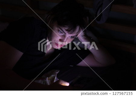 Young woman browsing smartphone in dark room at night 127567155