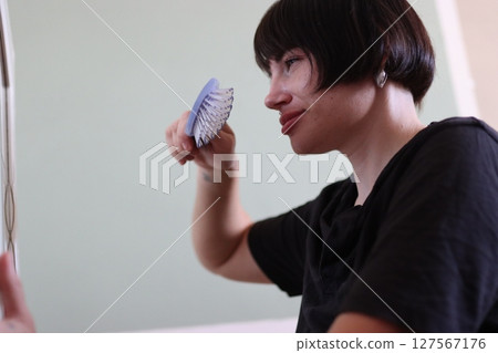 Hairdresser holding round hairbrush and looking in mirror 127567176