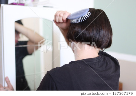 Woman brushing her bob haircut in front of mirror 127567179