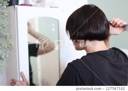 Young person combing hair in front of mirror at home 127567182