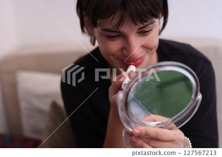 Smiling woman applying lipstick while holding small mirror 127567213