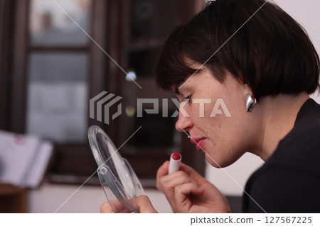 Woman applying red lipstick while looking in a mirror Woman applying red lipstick while looking in a mirror 127567225
