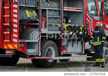 A firefighter meticulously prepares a modern firetruck for a mission to evacuate and respond to dangerous situations, showcasing the utmost dedication to safety and readiness in the face of a fire A firefighter meticulously prepares a modern firetruck for a mission to evacuate and respond to dangerous situations, showcasing the utmost dedication to safety and readiness in the face of a fire 127567226
