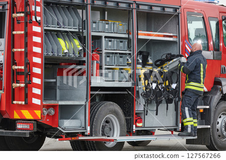 A firefighter meticulously prepares a modern firetruck for a mission to evacuate and respond to dangerous situations, showcasing the utmost dedication to safety and readiness in the face of a fire 127567266
