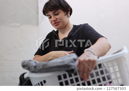 Young woman putting clothes into laundry basket at home Young woman putting clothes into laundry basket at home 127567303