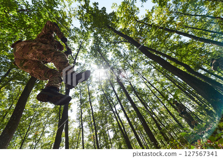 An elite soldier adeptly clears military barriers in the perilous wooded terrain, showcasing tactical skill and agility during specialized training An elite soldier adeptly clears military barriers in the perilous wooded terrain, showcasing tactical skill and agility during specialized training 127567341