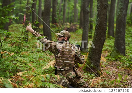 An elite soldier, camouflaged and stealthily navigating through dangerous woodland terrain, executes a covert mission in a secluded forest area 127567368