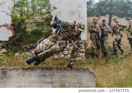 A highly trained elite military unit, clad in camouflage, skillfully navigates through perilous forest terrain, overcoming obstacles and executing a precise and covert mission 127567370