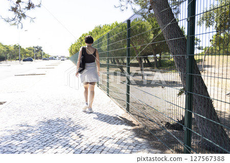 Woman walking on cobblestone street next to parking lot and fence 127567388