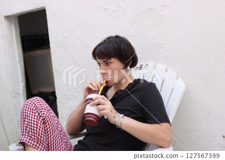 Young woman relaxing and drinking with straw on patio Young woman relaxing and drinking with straw on patio 127567399