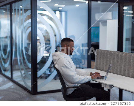 In a modern office setting, an African American businessman is diligently working on his laptop, embodying determination, ambition, and productivity in his professional environmen 127567535