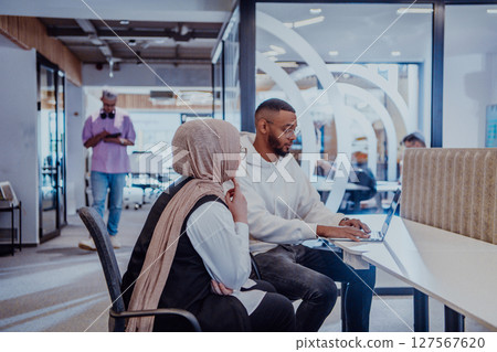 In a modern office setting, an African American businessman and his Muslim colleague, wearing a hijab, engage in collaborative discussions, tackling various business tasks and solving problems 127567620