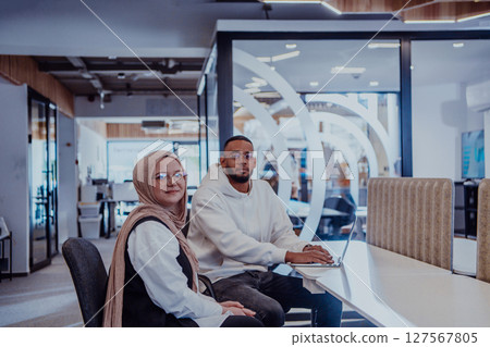 In a modern office setting, an African American businessman and his Muslim colleague, wearing a hijab, engage in collaborative discussions, tackling various business tasks and solving problems 127567805