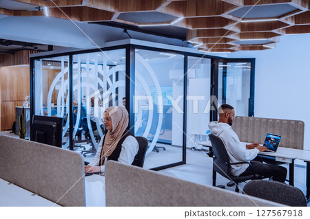 In a modern office setting, an African American businessman and his Muslim colleague, wearing a hijab, engage in collaborative discussions, tackling various business tasks and solving problems 127567918