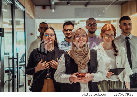 A group of young business professionals stands together, taking a well-deserved break from their busy workday, showcasing camaraderie, teamwork, and a moment of relaxation in their dynamic workplace 127567933