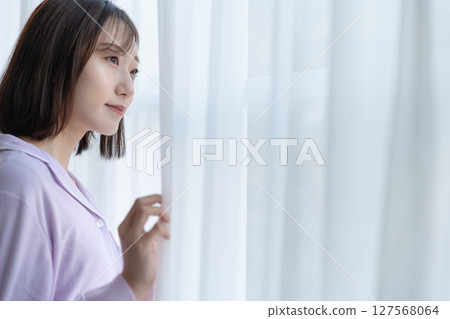Young woman looking outside through a gap in lace curtains Young woman looking outside through a gap in lace curtains 127568064