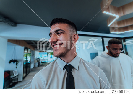 A group of young business professionals stands together, taking a well-deserved break from their busy workday, showcasing camaraderie, teamwork, and a moment of relaxation in their dynamic workplace 127568104